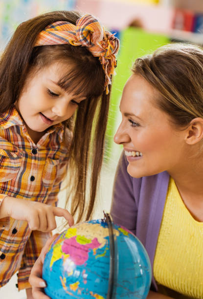 istock Happy preschool teacher analyzing a globe with small girl in kindergarten 1133548389