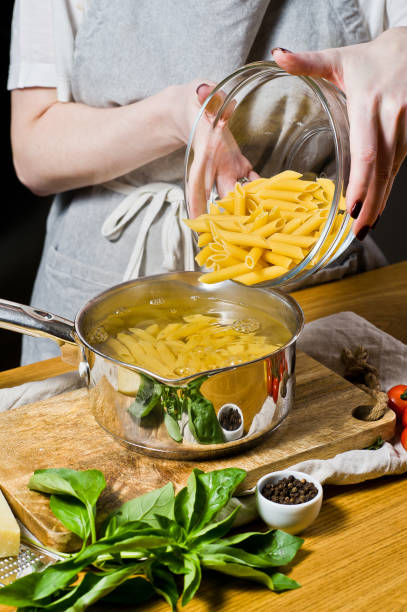 The chef pours the pasta Penne in a pot of boiling water. black background, side view, space for text.