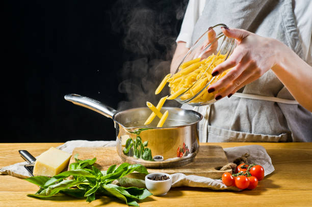 The chef pours the pasta Penne in a pot of boiling water. black background, side view, space for text.