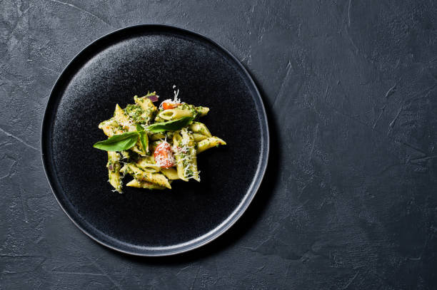 istock Italian pasta Penne with spinach, cherry tomatoes and Basil. Black background, top view, space for text. 1133551336
