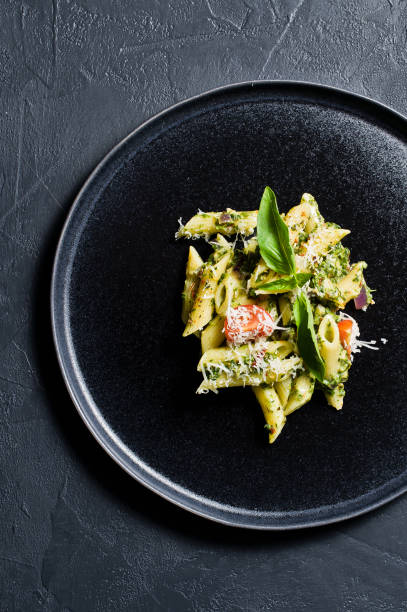 istock Italian pasta Penne with spinach, cherry tomatoes and Basil. Black background, top view, space for text. 1133551337