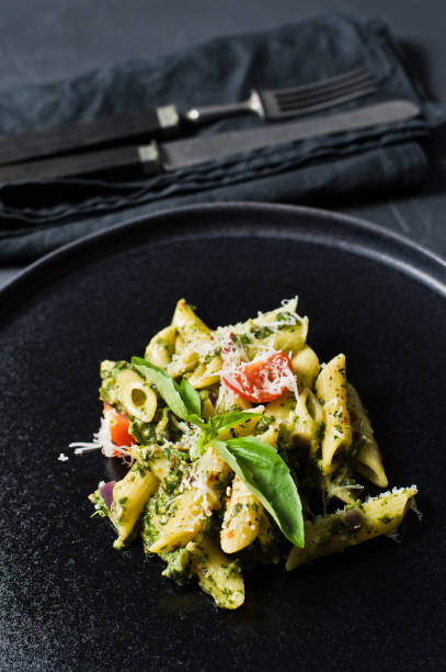 istock Italian pasta Penne with spinach, cherry tomatoes and Basil. Black background, side view, close-up. 1133551358