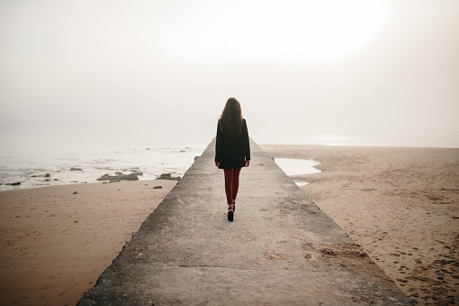 A rear view of a young woman walking on a pier by the sea