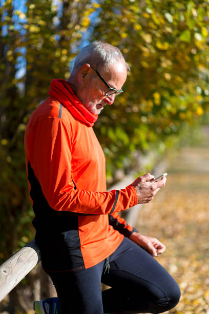 istock Side view of a senior runner man leaning on fence while testing exercise in a mobile phone outdoors in a sunny day 1133555537