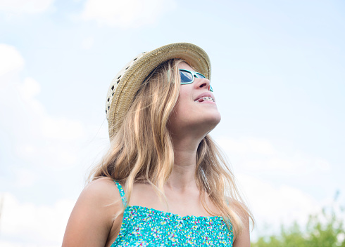 Travel, summer holidays, vacation and people concept.  Smiling happy girl in sun hat and sunglasses over blue sky background.