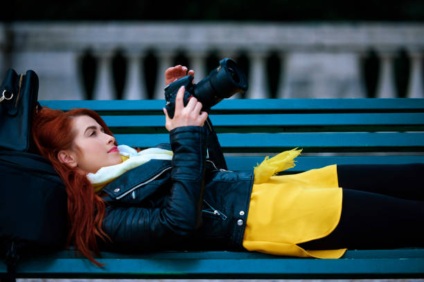 lifestyle shot of young photographer woman lying on bench with her camera.