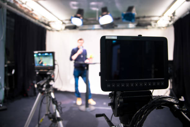 istock Journalist in a television studio is talking into a microphone, blurry film cameras 1133560162