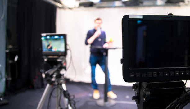 Journalist in a television studio is talking into a microphone, blurry film cameras