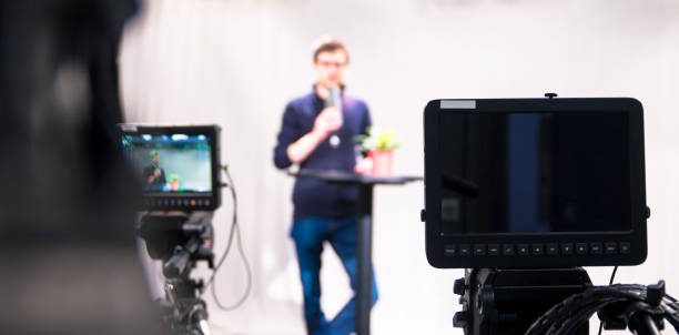 istock Journalist in a television studio is talking into a microphone, blurry film cameras 1133560184