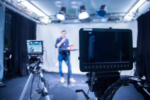 istock Journalist in a television studio is talking into a microphone, blurry film cameras 1133560187