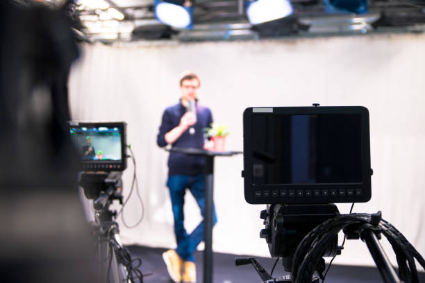 istock Journalist in a television studio is talking into a microphone, blurry film cameras 1133560189