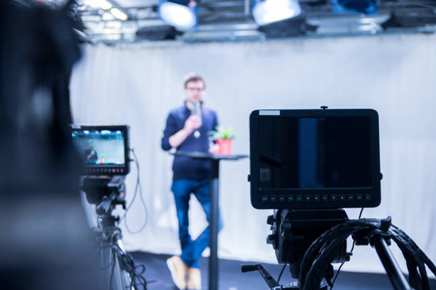 istock Journalist in a television studio is talking into a microphone, blurry film cameras 1133560198