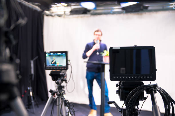 istock Journalist in a television studio is talking into a microphone, blurry film cameras 1133560209
