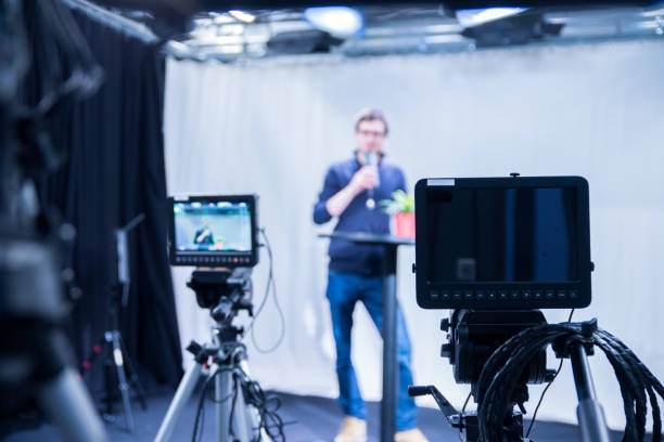 istock Journalist in a television studio is talking into a microphone, blurry film cameras 1133560215