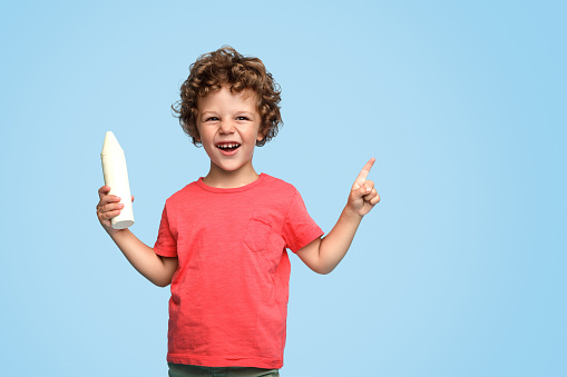 Adorable curly boy holding big piece of chalk having idea and smiling on blue background