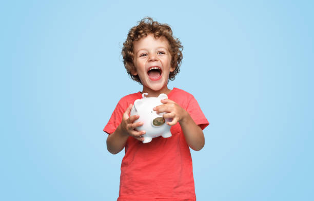 Excited boy with piggy bank Cute little boy with piggy bank laughing and looking at camera while standing on blue background only boys stock pictures, royalty-free photos & images