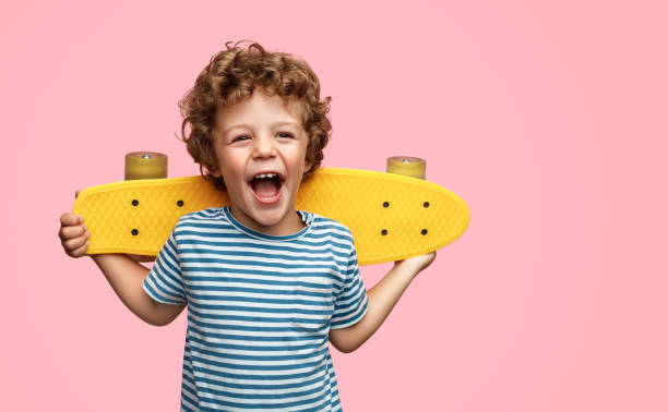 Cute boy with yellow skateboard Funny little boy holding yellow skateboard on shoulders and screaming while standing on pink background only boys stock pictures, royalty-free photos & images