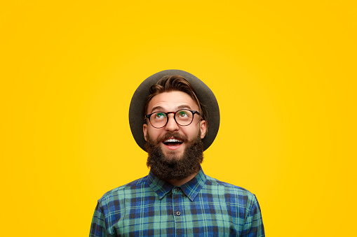 Amazed young hipster in shock looking up with surprise standing on bright yellow backdrop