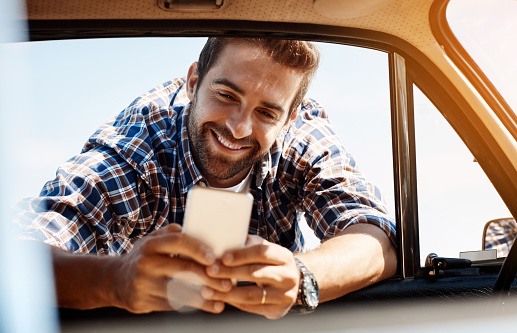 Cropped shot of a handsome man sending a text while enjoying a road trip