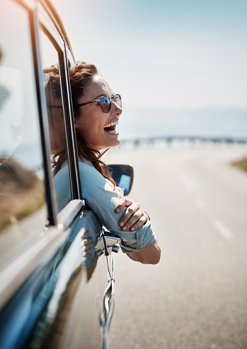 Cropped shot of an attractive woman hanging out of a car window while enjoying a road trip