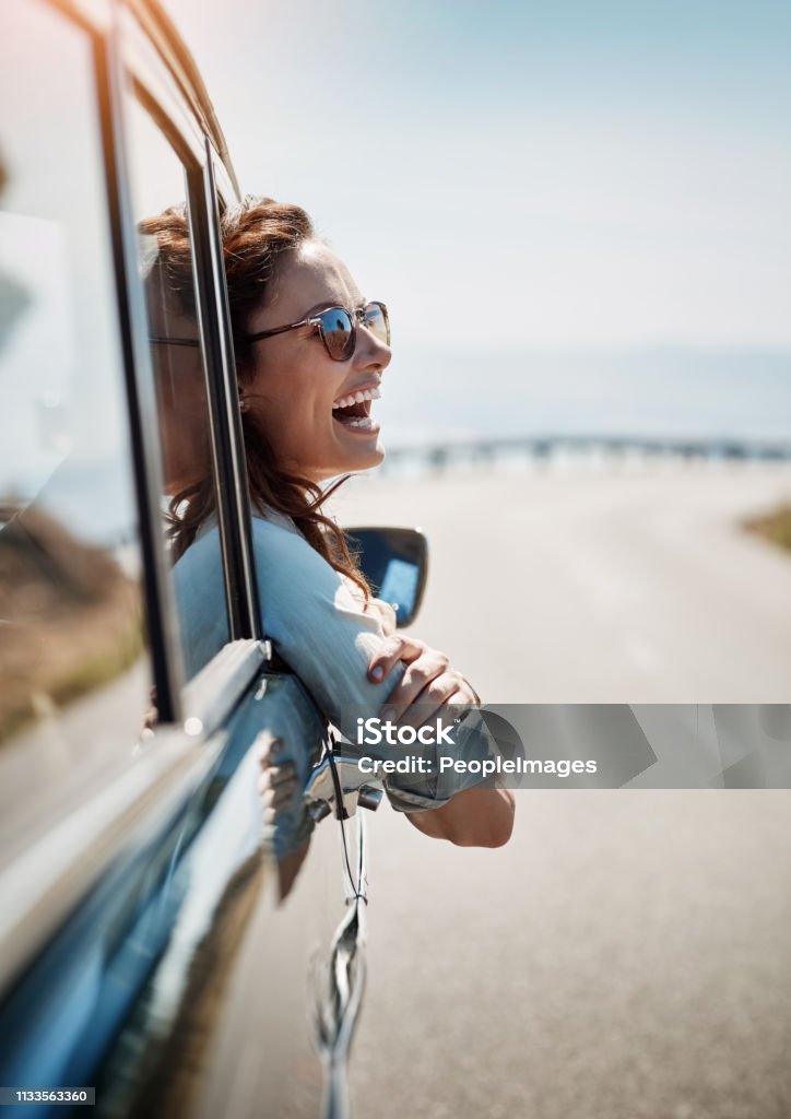 Road trips put me in a happy mood Cropped shot of an attractive woman hanging out of a car window while enjoying a road trip Car Stock Photo