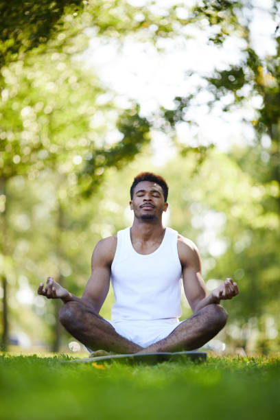 istock Serious black man with crossed legs meditating in park 1133568302