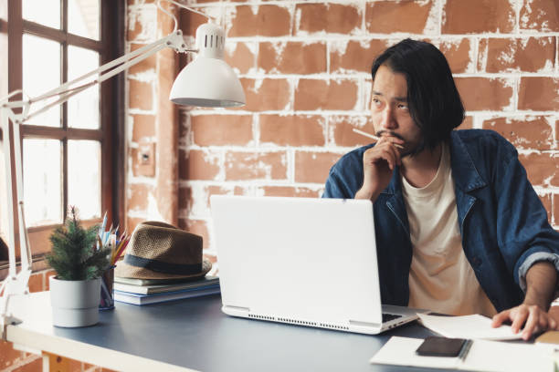istock Young Asian man thinking and working on laptop for business creative designer 1133573052