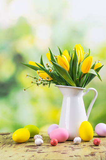 Directly above of chicken Easter eggs placed on basket with colorful feathers and yellow flowers.