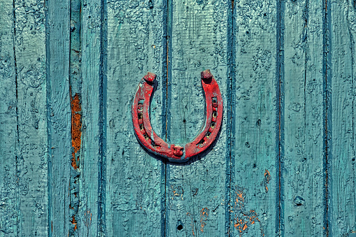 Red horseshoe hanging on an old wooden surface painted dark turquoise paint