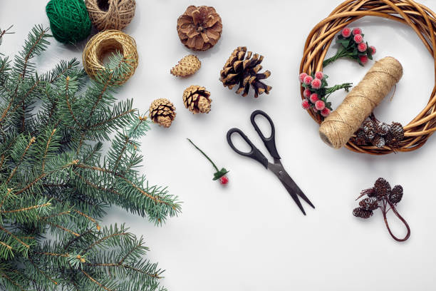 istock Beautiful festive handmade wreath base with three bumps near it, threads and twigs blue Christmas tree on the white table background, flat lay. 1133576910