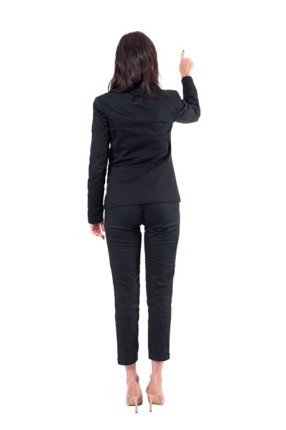 istock Rear view of elegant business woman in black suit pointing finger using interactive touch screen button. 1133577132