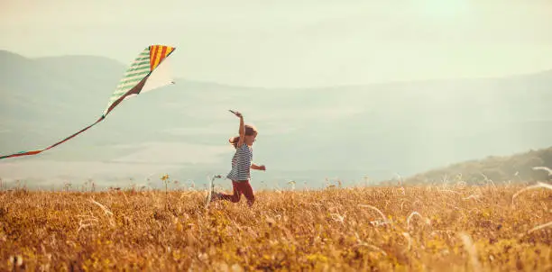 Photo of happy child girl running with kite at sunset outdoors