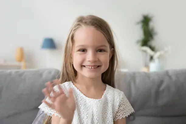 Photo of Smiling little girl looking at camera, waving hand, greeting