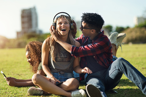 Shot of a two cheerful young friends listening to music on headphones outside on a park during the day