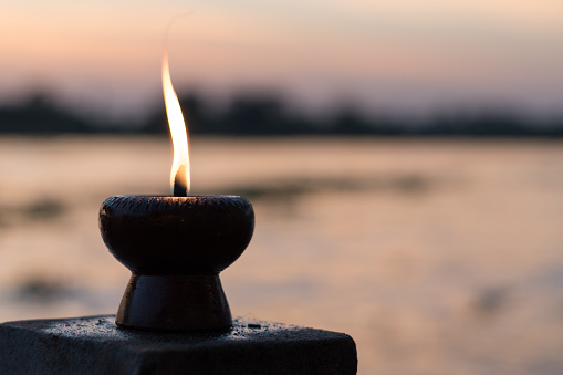 Candle light fire lamp nearby abstract background river during sunset or sunrise in countryside. Melting candlestick in evening twilight. Religion abstract concept.