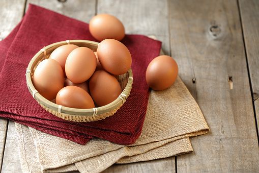 Fresh eggs stacked in a bamboo basket on wooden table; Top view.