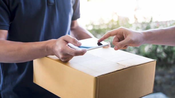 istock Delivery mail man giving parcel box to recipient, Young man appending signing in digital mobile phone receipt of delivery package from post shipment courier at home 1133587400