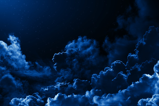 Mystical midnight sky with stars surrounded by dramatic clouds. Dark natural background with night starry cloudy sky. Moonlit clouds