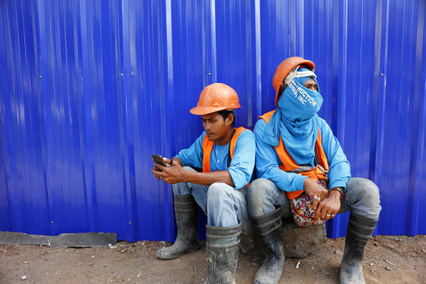 ANTIPOLO CITY, PHILIPPINES - MARCH 1, 2019: Workers at a construction site take a break and sit in front of a blue wall.