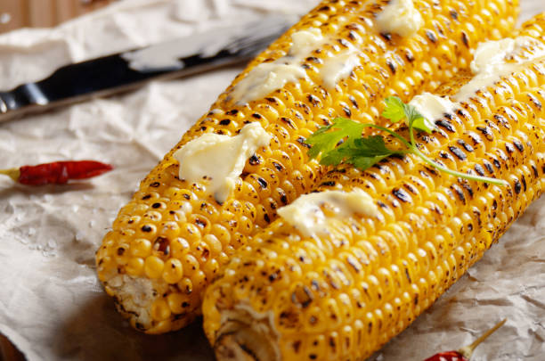 istock Kitchen table with grilled sweet corn cob under melting butter and greens on baking paper 1133593808