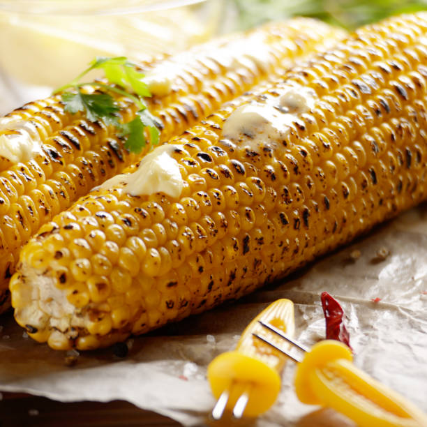 istock Kitchen table with grilled sweet corn cob under melting butter and greens on baking paper 1133593818