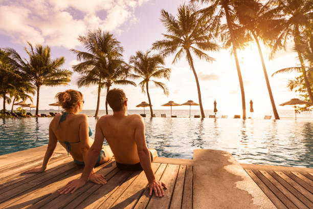 pareja disfrutando de vacaciones en la playa en el complejo tropical con piscina y palmeras de coco cerca de la costa con hermoso paisaje al atardecer, destino de luna de miel - honeymoon fotografías e imágenes de stock