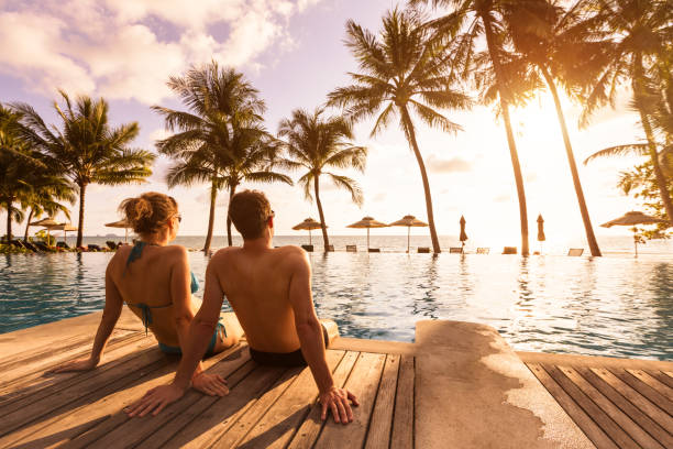 Photo of Couple enjoying beach vacation holidays at tropical resort with swimming pool and coconut palm trees near the coast with beautiful landscape at sunset, honeymoon destination