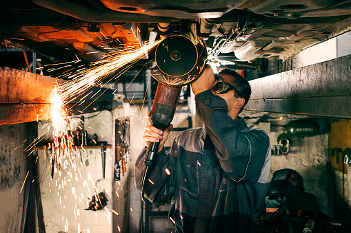 Mechanic using grinding wheel on car bottom making sparks