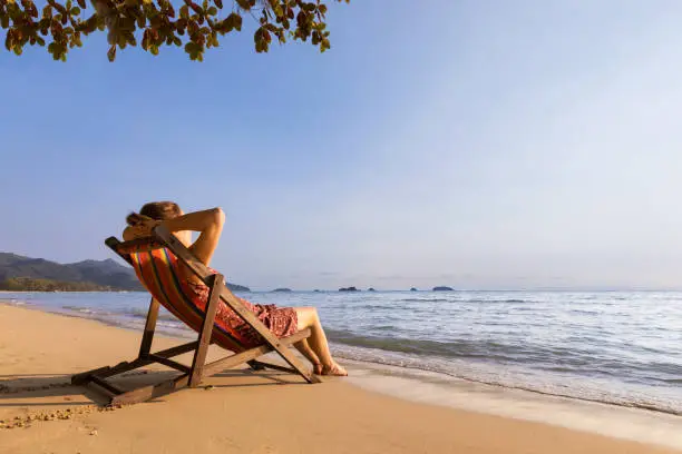 Woman enjoying vacation holidays on the beach and relaxing in a deckchair near the sea, warm sunny summer day for resting and sunbathing