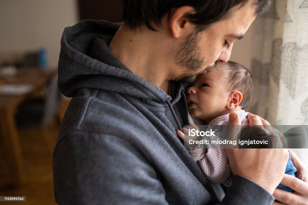 Proud father kissing newborn son Young father holding newborn baby boy in arms, gently kissing baby boy in head Father Stock Photo