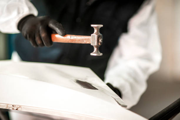 Body shop repairman using a hammer to straighten out a surface on a deformed car segment in a body shop Car repair technician using a hammer to flatten a surface on a deformed car part in a repair shop. door panel stock pictures, royalty-free photos & images