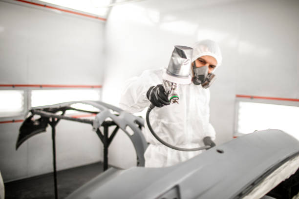 istock Car painter in white overalls spraying a car body with paint 1133601327