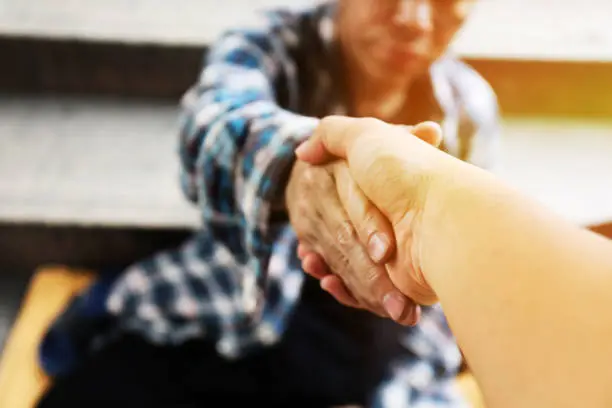 Photo of Close-up handshake for help homeless man on walking street in the capital city.