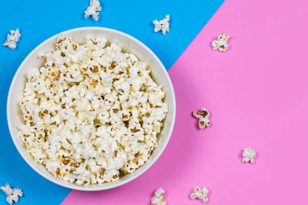 istock White bowl of popcorn on a bright pink and blue background with scattered popcorn, copy space. 1133602890